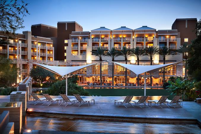 Resort terrace and lounge seating at dusk with lit guest rooms and palms
